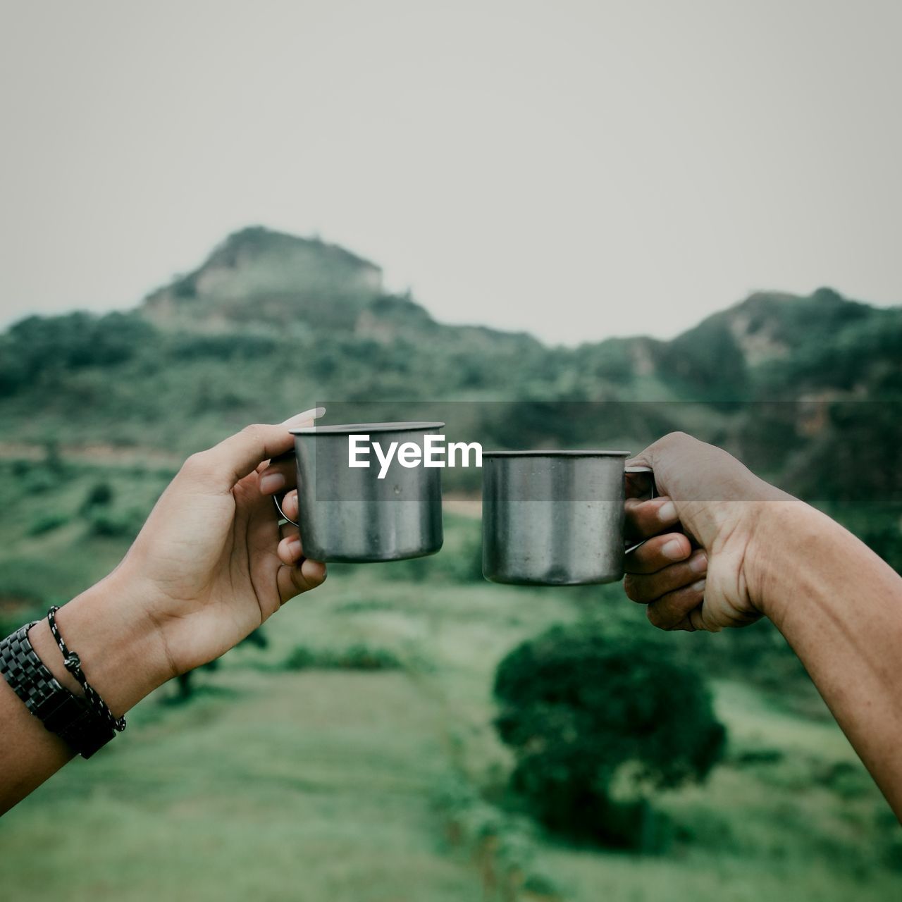 CROPPED IMAGE OF HAND HOLDING DRINK AGAINST MOUNTAINS