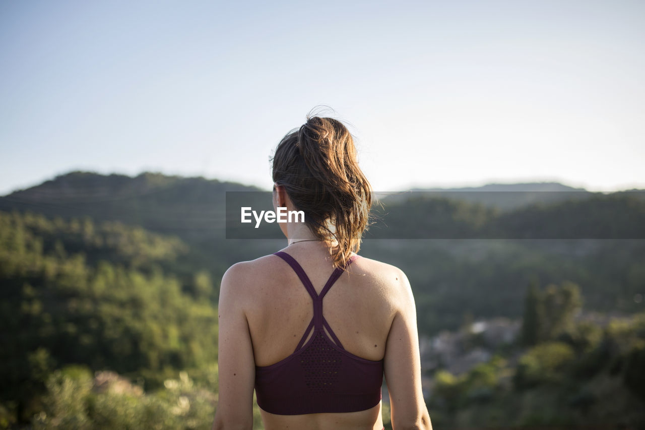 REAR VIEW OF WOMAN LOOKING AT CAMERA AGAINST SKY