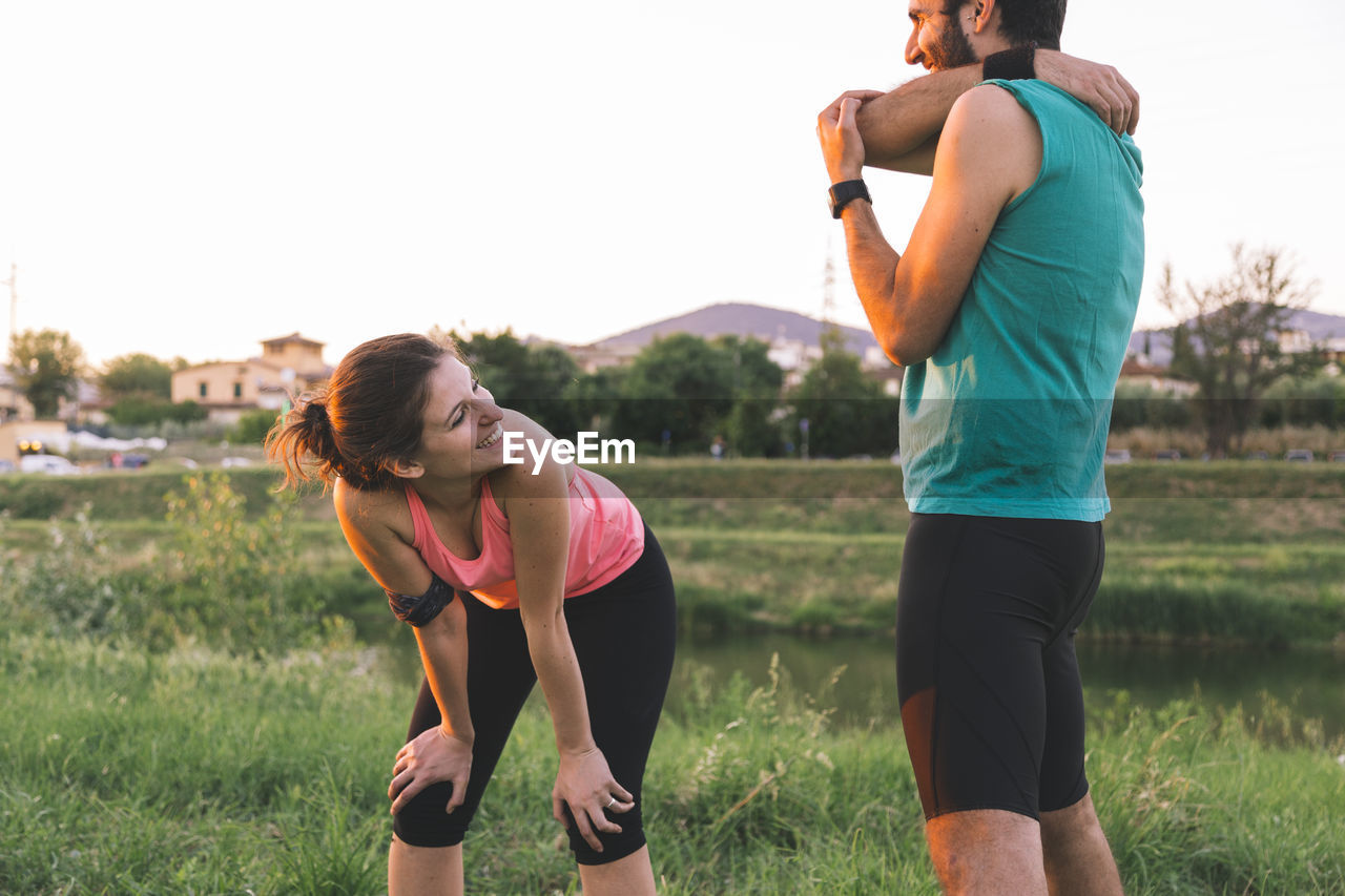 Smiling active couple relaxing after jogging in park during sunset