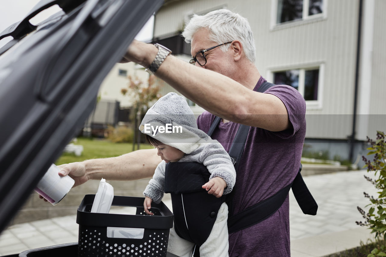 Smiling mature man with baby putting rubbish into bin