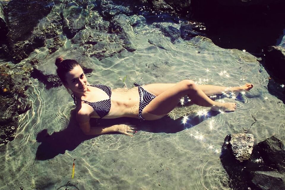 Portrait of woman wearing bikini lying down in water