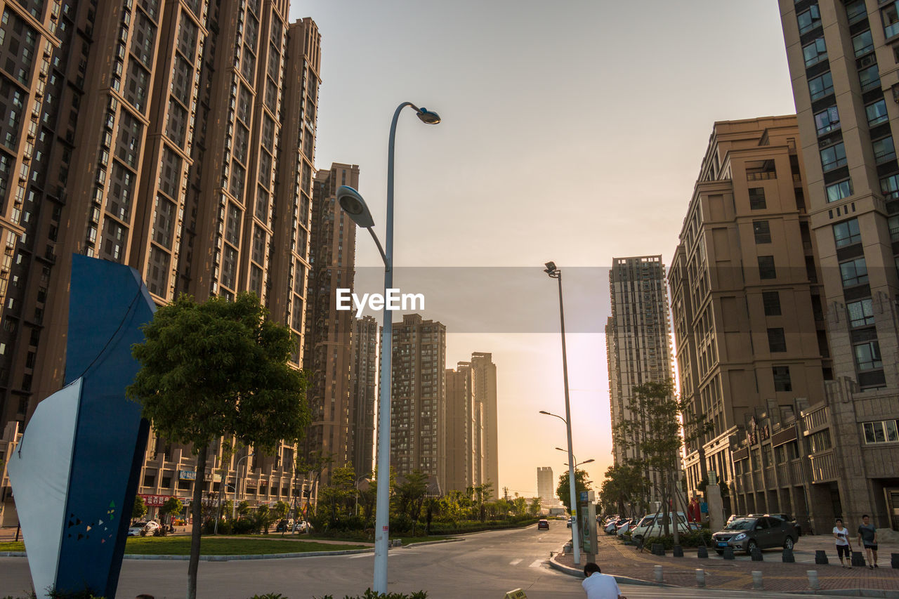 Road amidst buildings against sky during sunset in city