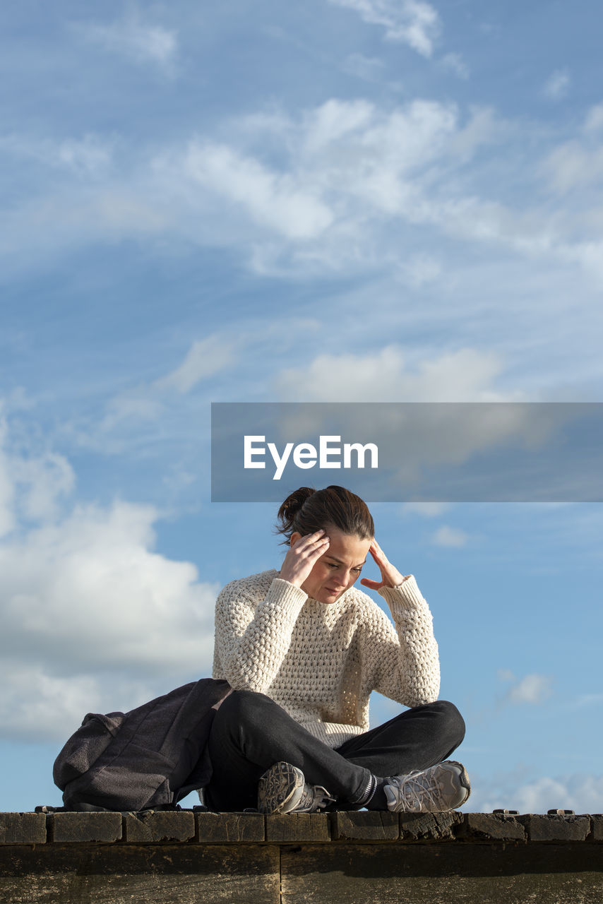 Woman sitting outside with her head in her hand, looking upset or down.