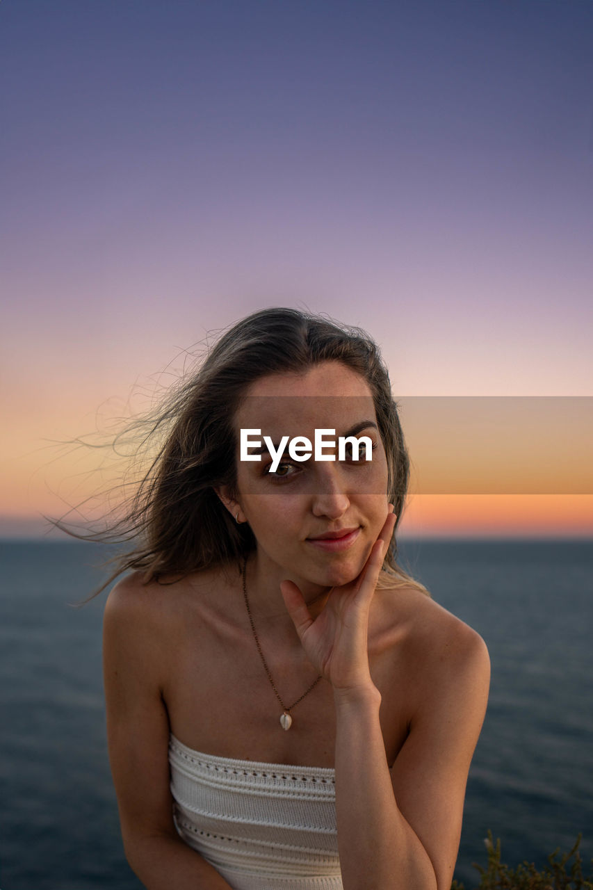 adult, portrait, one person, women, sky, water, sea, female, sunset, nature, hairstyle, looking at camera, land, long hair, beach, beauty in nature, brown hair, person, smiling, young adult, emotion, waist up, photo shoot, sunlight, clothing, holiday, dusk, portrait photography, happiness, lifestyles, outdoors, vacation, front view, trip, leisure activity, fashion, summer, looking, horizon over water, tranquility, copy space, relaxation, standing, travel, human face, blue, horizon