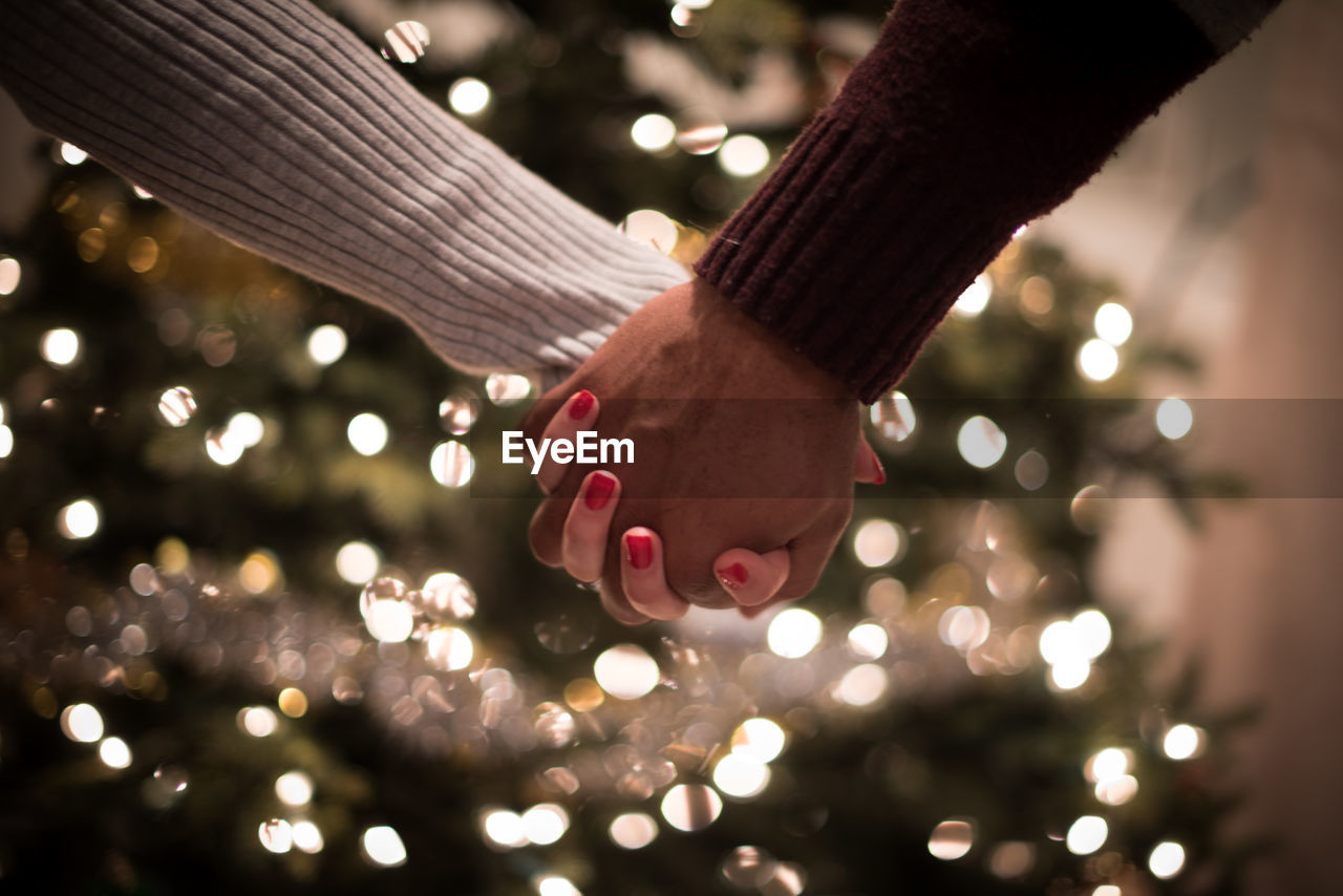Cropped image of couple holding hands against christmas tree