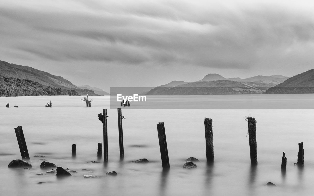 water, black and white, mountain, scenics - nature, sky, monochrome photography, monochrome, beauty in nature, environment, horizon, nature, sea, land, ocean, landscape, cloud, tranquility, tranquil scene, shore, no people, coast, wood, post, beach, mountain range, wooden post, reflection, travel, outdoors, travel destinations, wave, bay, day, non-urban scene