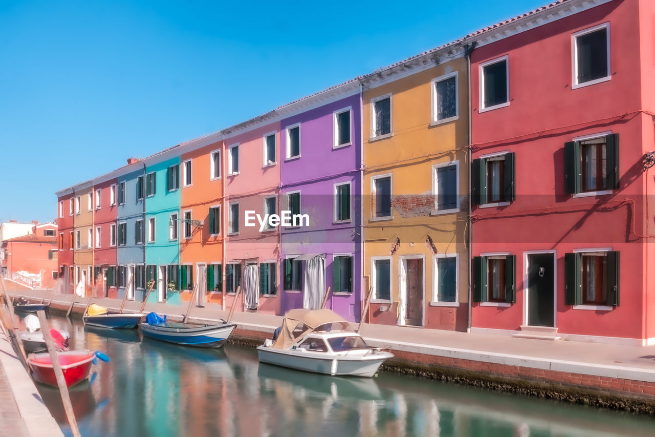 Boats moored in canal by buildings against sky