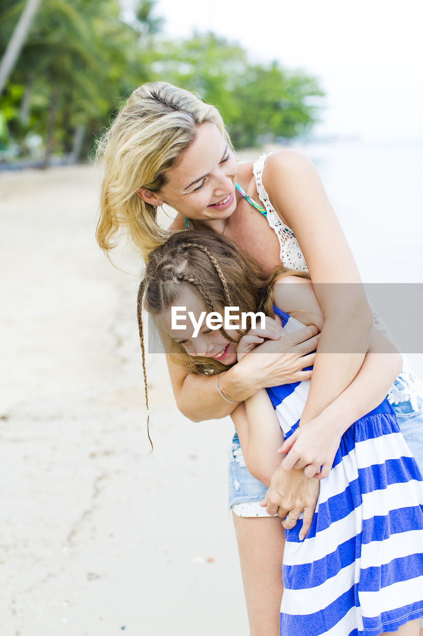 Happy mother and daughter standing at beach