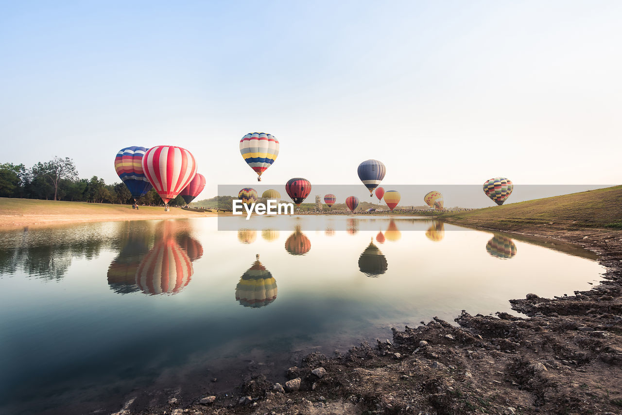 Reflection of hot air balloons on lake against sky