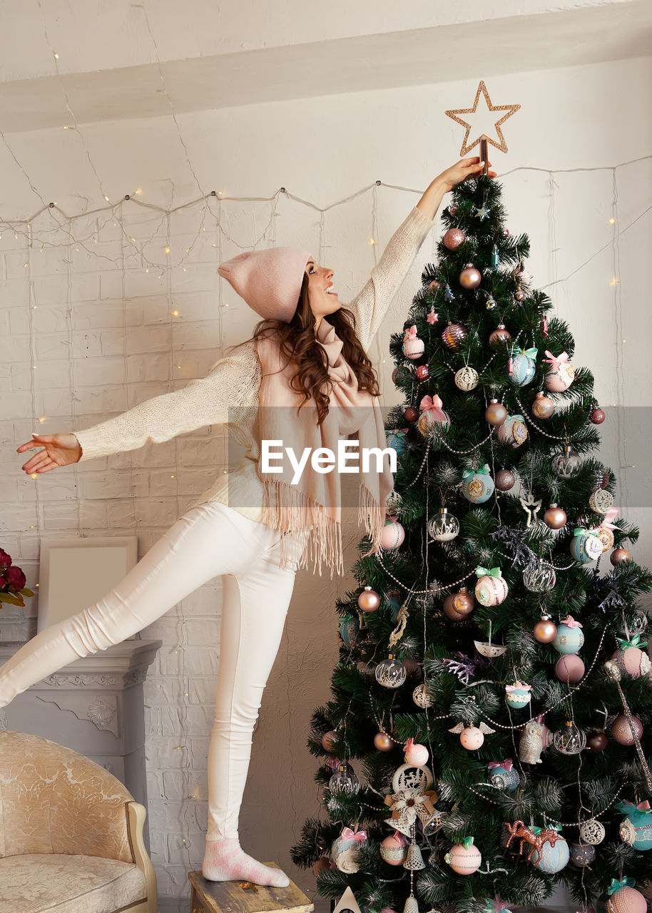 Happy young woman decorates the christmas tree. a girl in a sweater sets a star on top of a