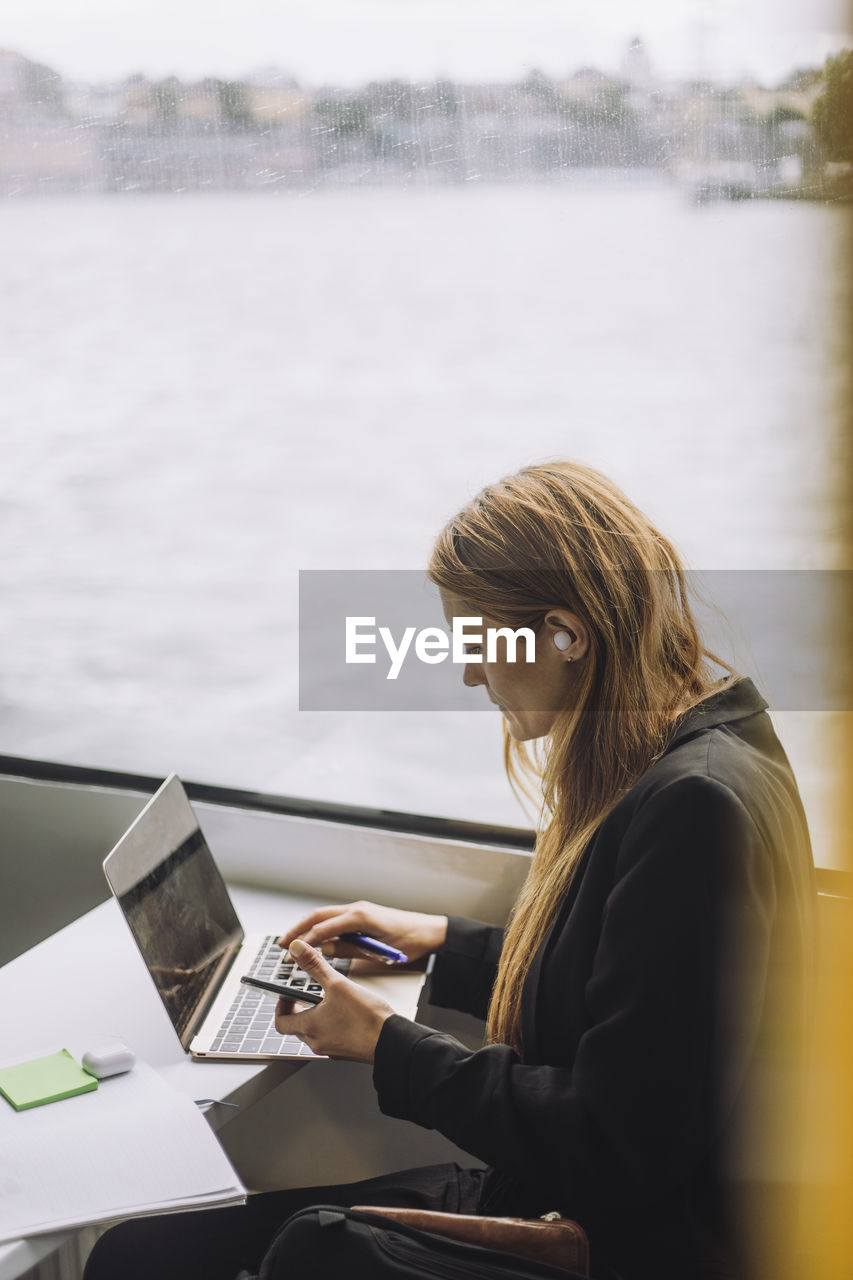 Side view of female freelancer using laptop while sitting in ferry