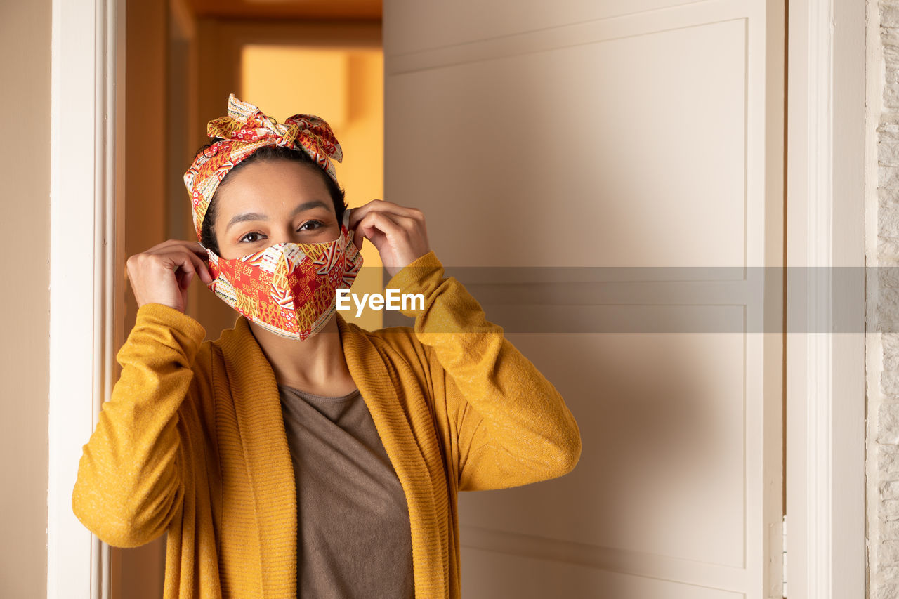 Portrait of smiling woman wearing mask standing at home