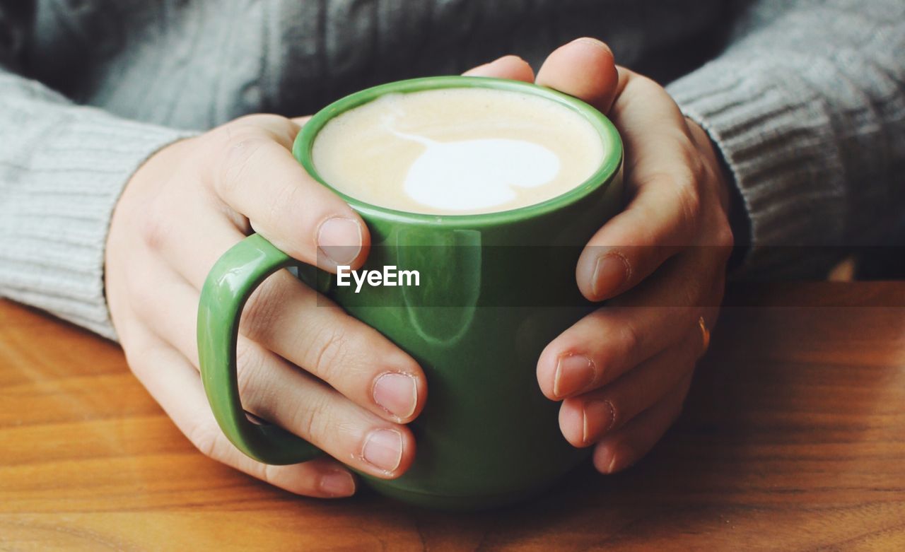 Close-up of hands holding coffee cup on table