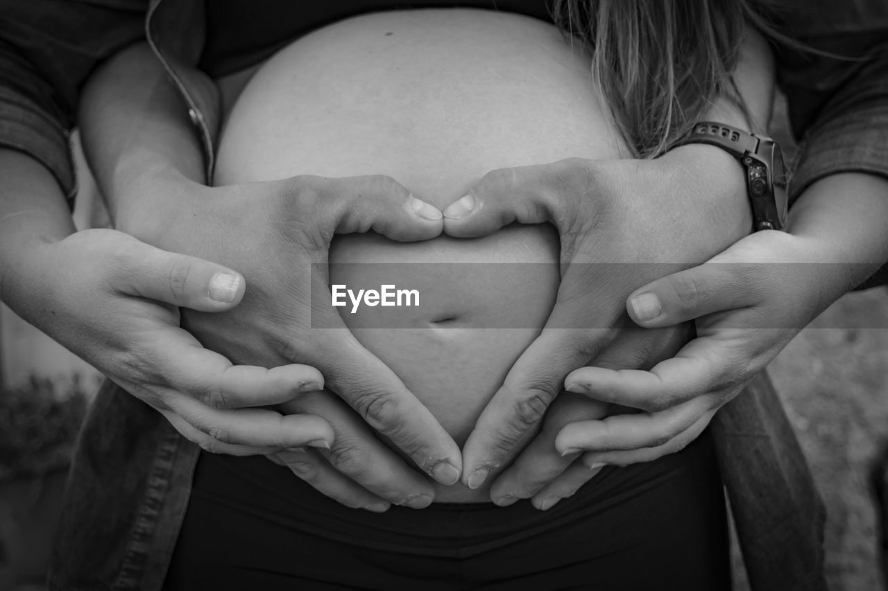 Midsection of pregnant woman with man making heart shape on stomach