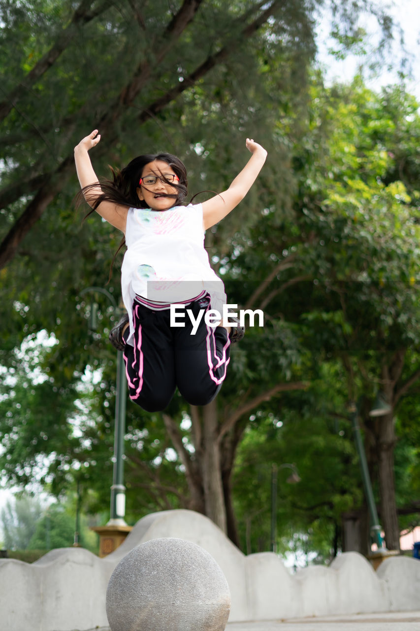 Full length of woman jumping against trees