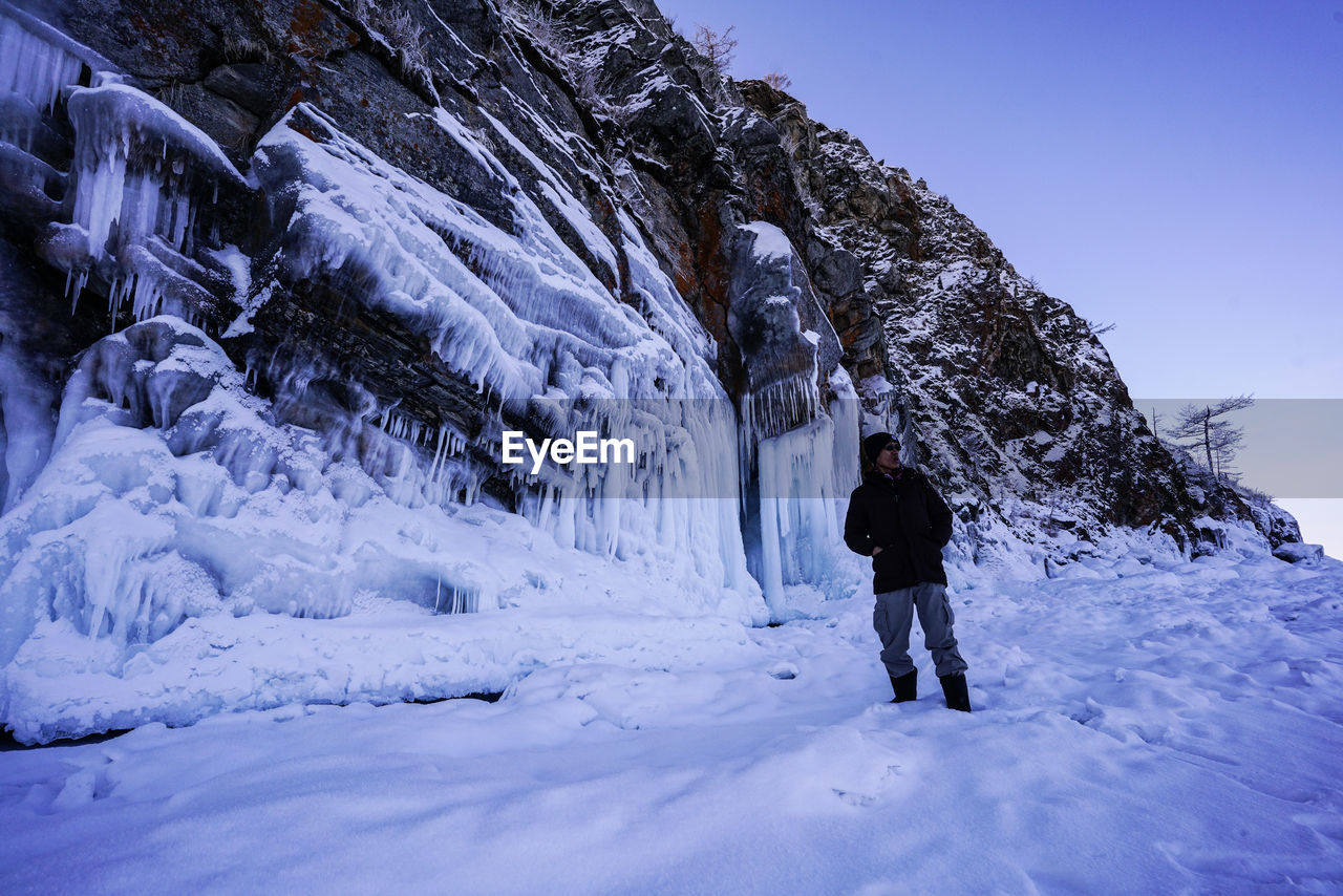 REAR VIEW OF PERSON STANDING ON SNOW COVERED MOUNTAIN