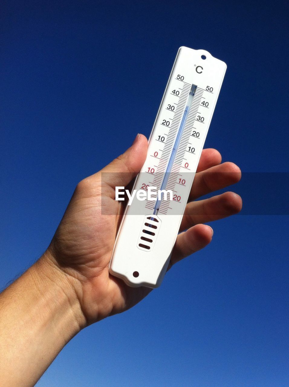 Cropped image of hand holding thermometer against clear sky