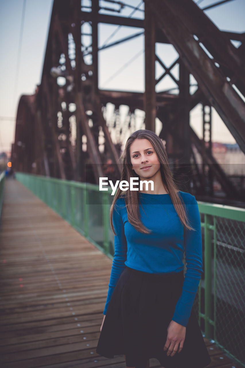 Beautiful young woman with long healthy dark blonde hair in blue long sleeve shirt and black skirt