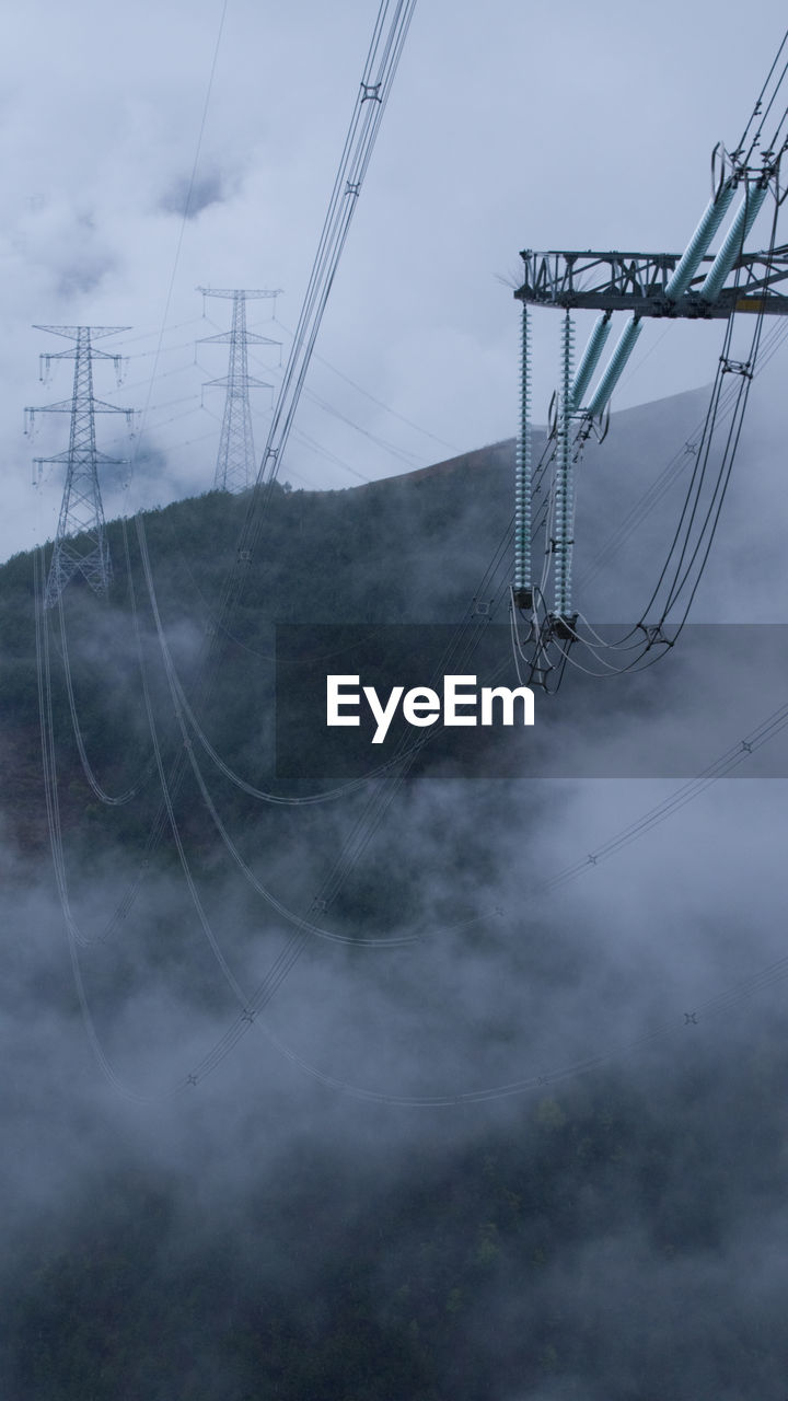 Low angle view of electricity pylon against cloudy sky