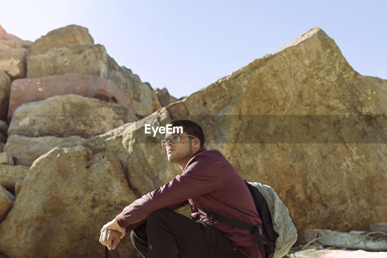 Low angle view of man sitting on mountain against clear sky