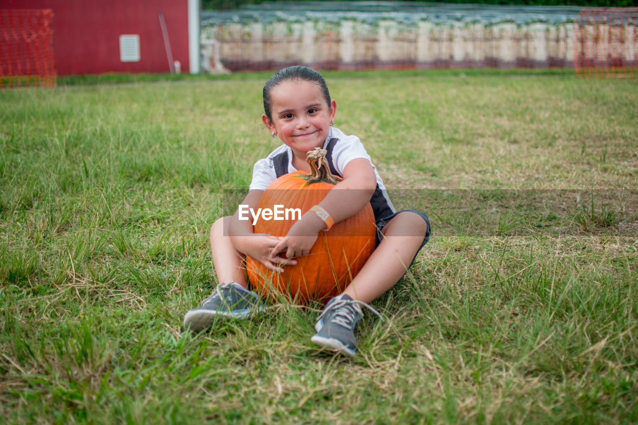 Portrait of smiling girl sitting with pumpkin on grassy field