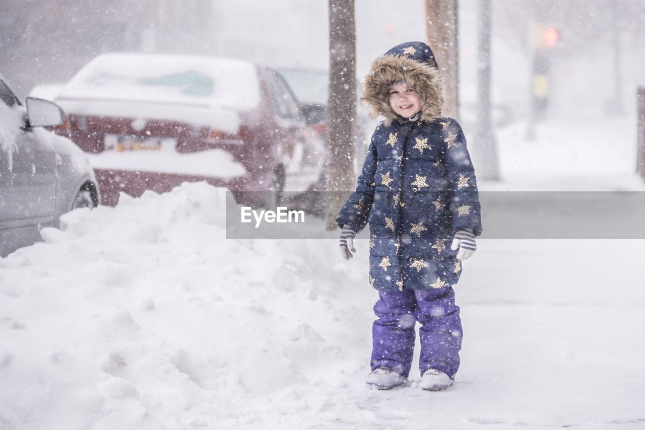 Portrait of smiling child standing on snowy sidewalk