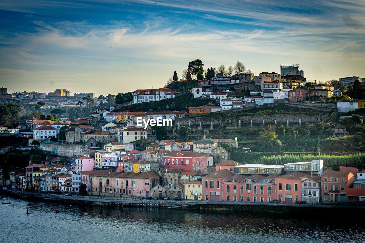 River amidst buildings in town against sky at sunset