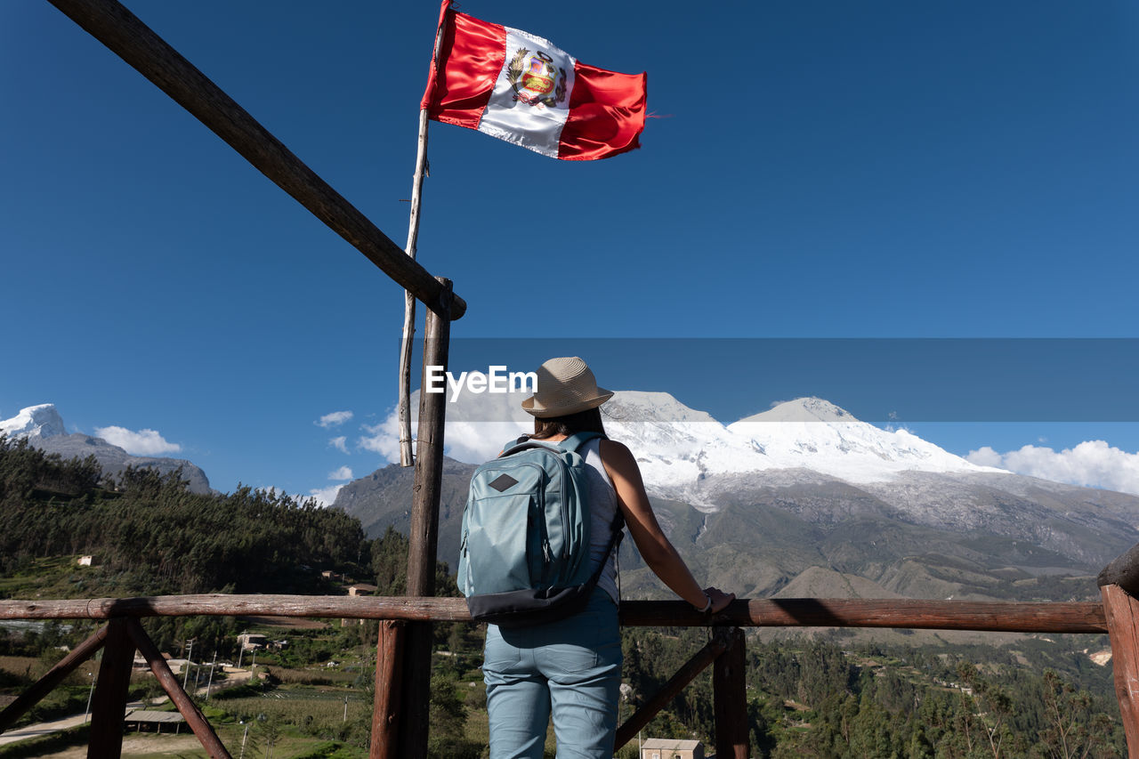 Tourist at a viewpoint with a peruvian flag observes the mountain named huascaran.