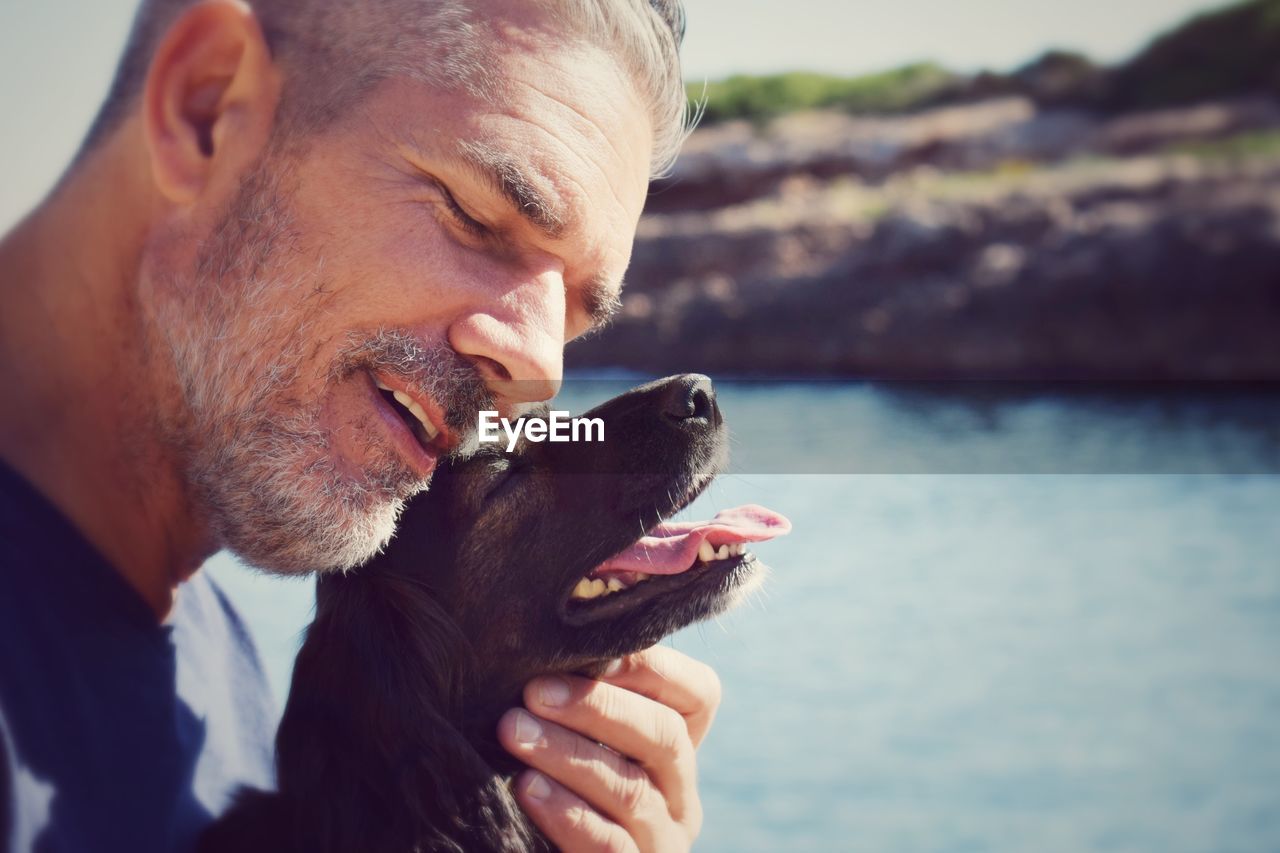 Close-up of happy man with dog against river