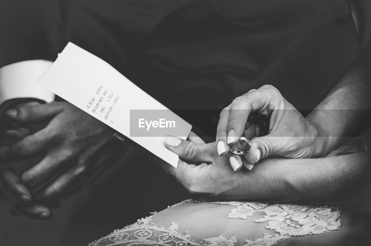Midsection of bride holding ring and paper with text while sitting by groom