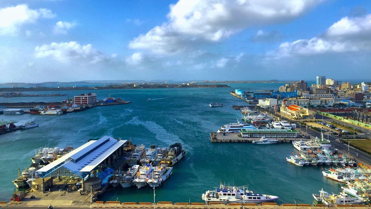 High angle view of ships moored at harbor against cloudy sky