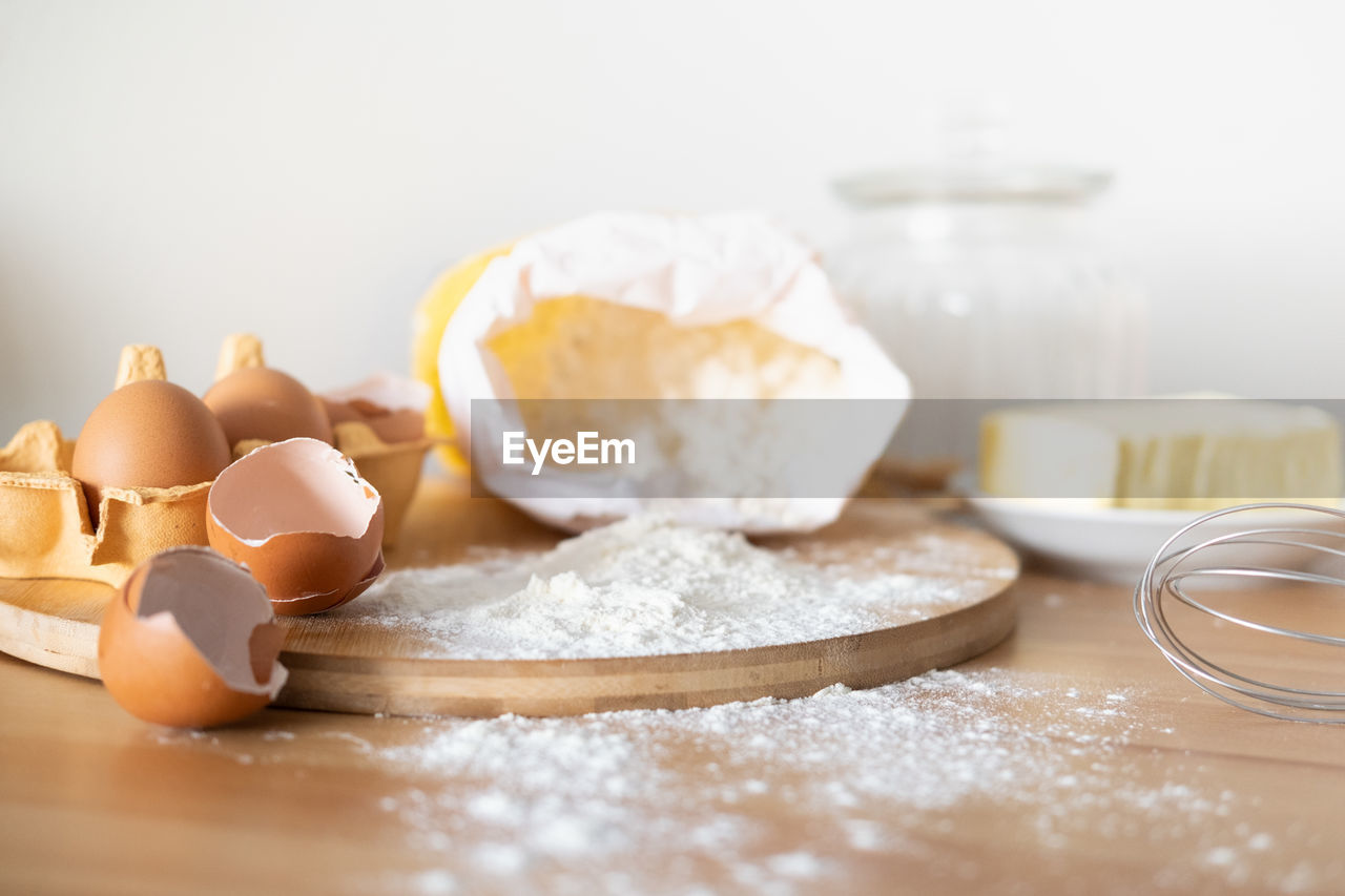 Baking cake or cupcakes ingredients - butter, flour, whisk, eggs and eggshells on wooden chalkboard