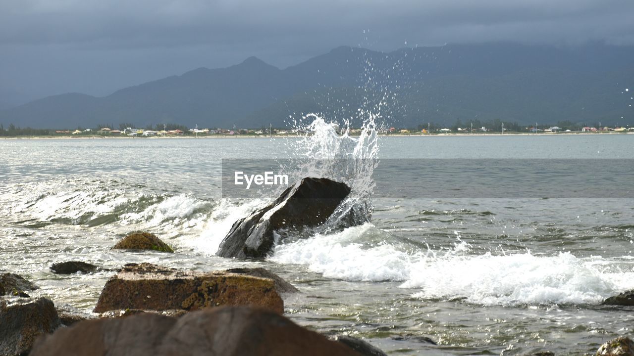 WATER SPLASHING IN SEA AGAINST MOUNTAINS