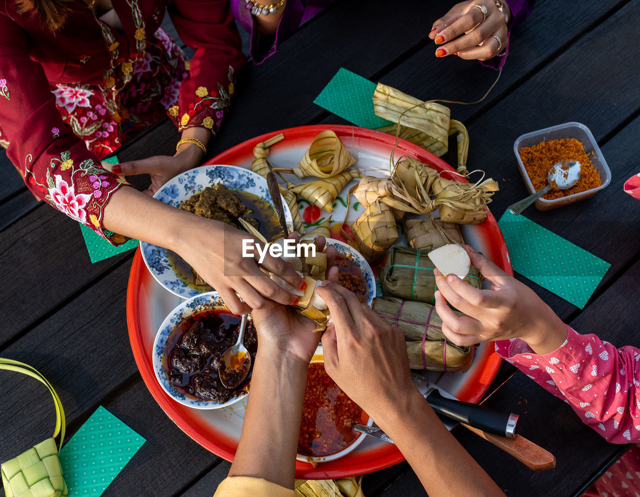 Top view of hands, muslim family, enjoying traditional malay cuisines on tray, at end of ramadan

