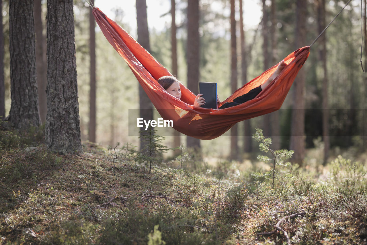 Teenage girl reading book in hammock in forest