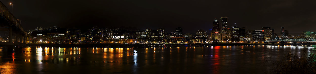 Illuminated cityscape by river against sky at night