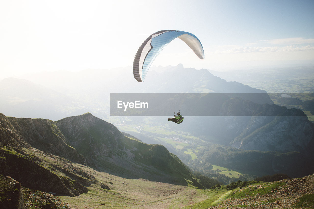 View of man paragliding over landscape against sky