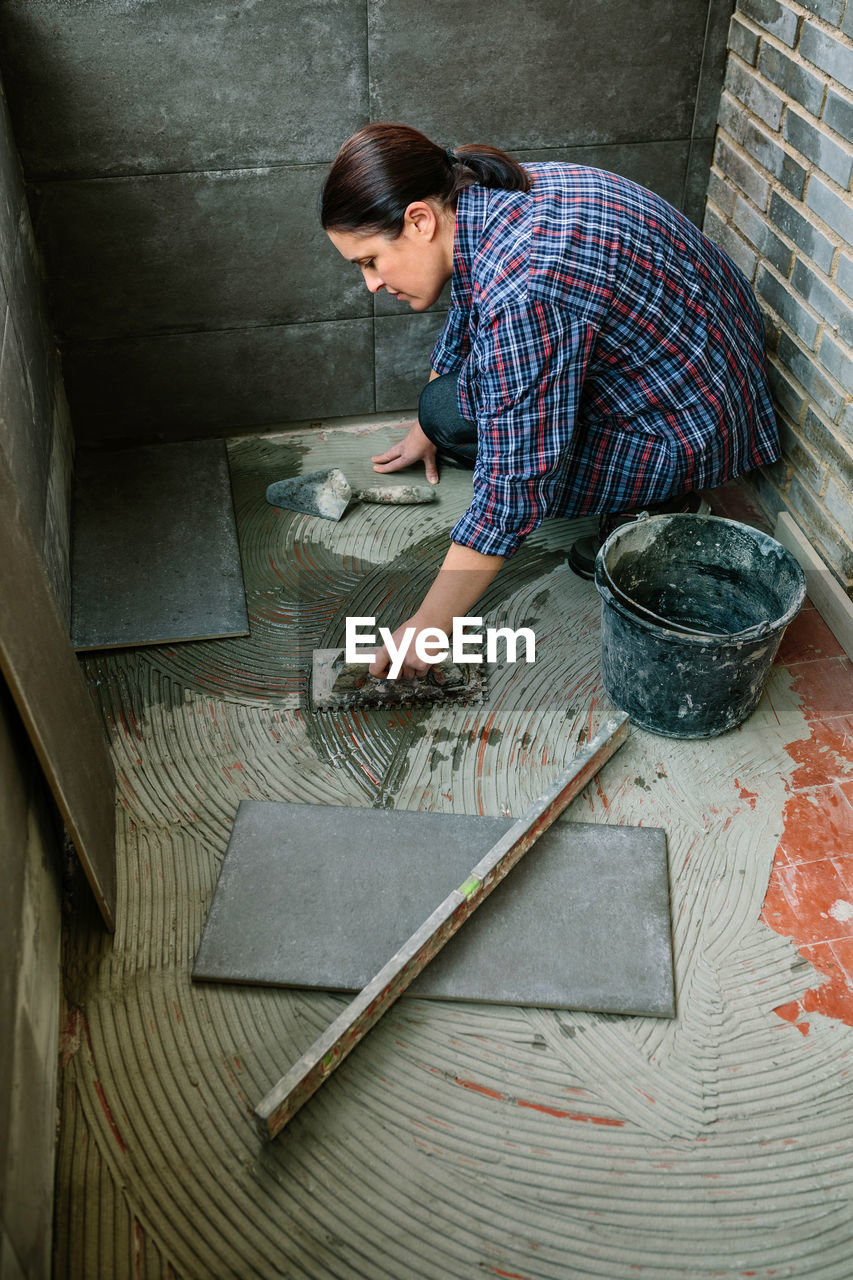 High angle view of mason installing tiles on floor