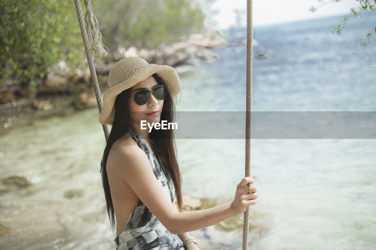 Young woman sitting on swing against sea