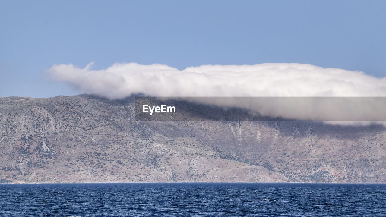 Scenic view of sea by mountain against sky