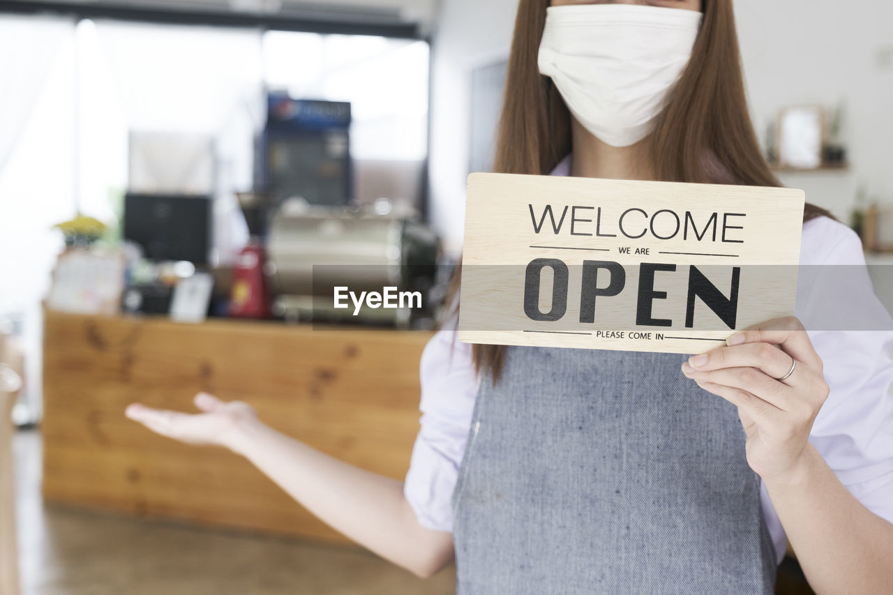 Midsection of woman holding signboard at cafe