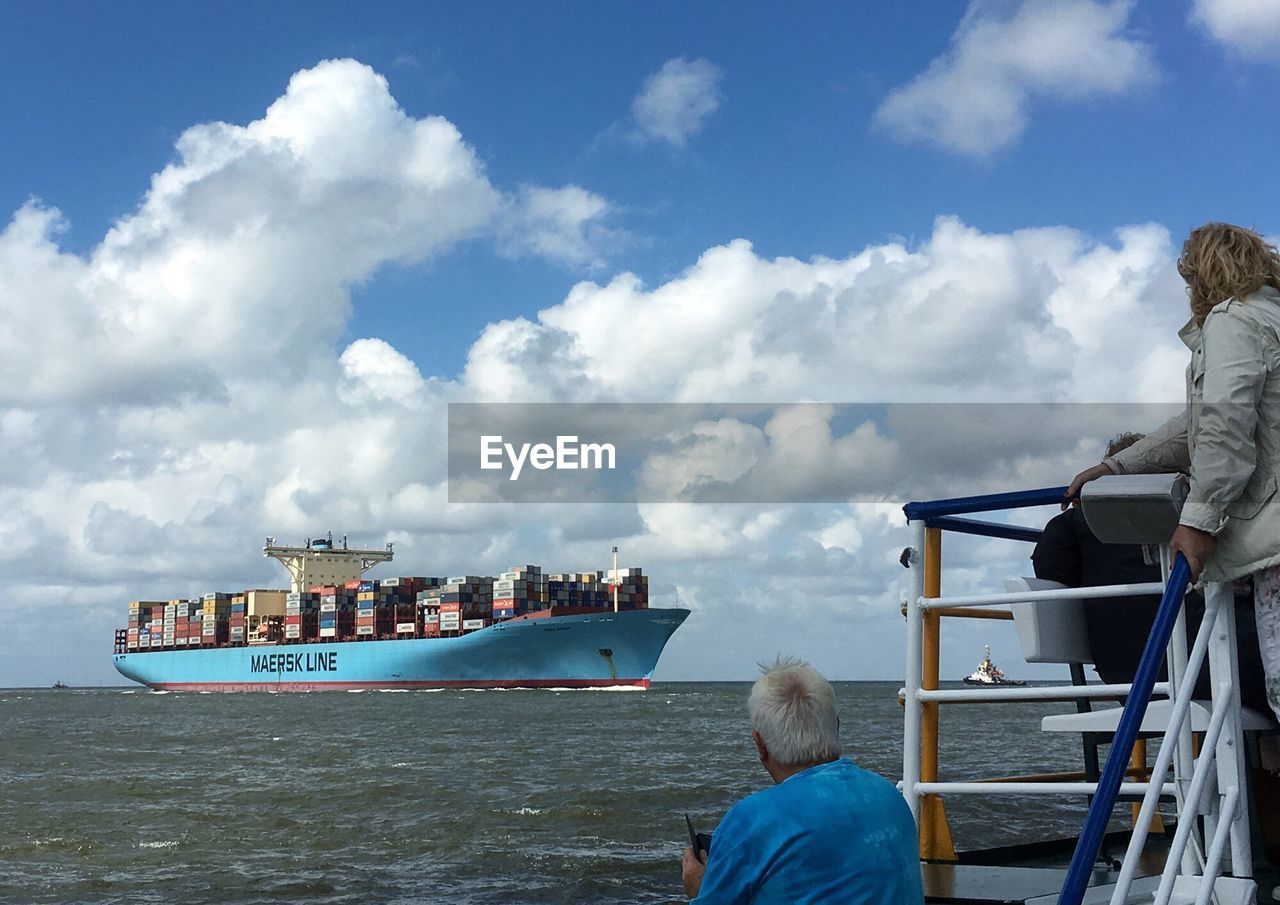 Rear view of man with woman looking at container ship in sea against sky