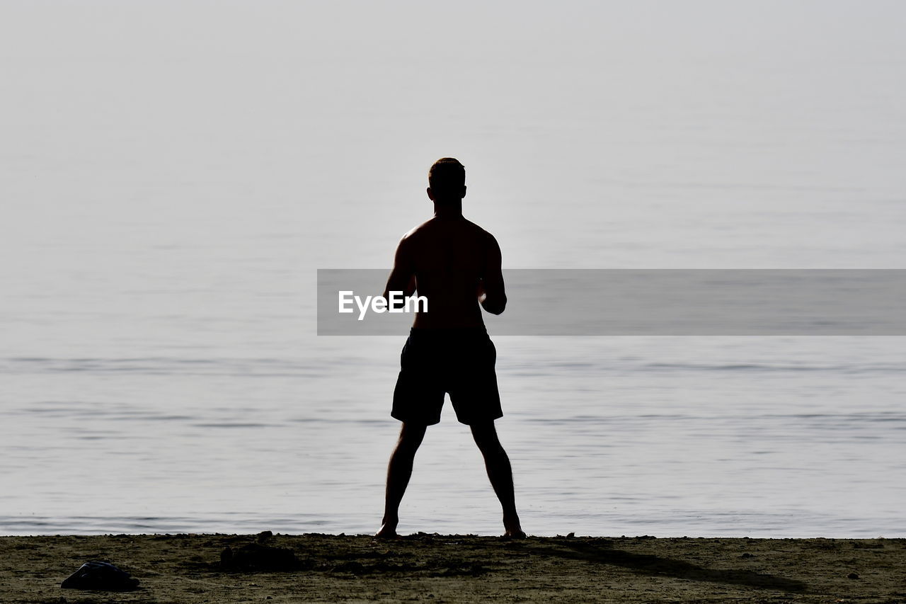 REAR VIEW OF MAN STANDING ON SHORE