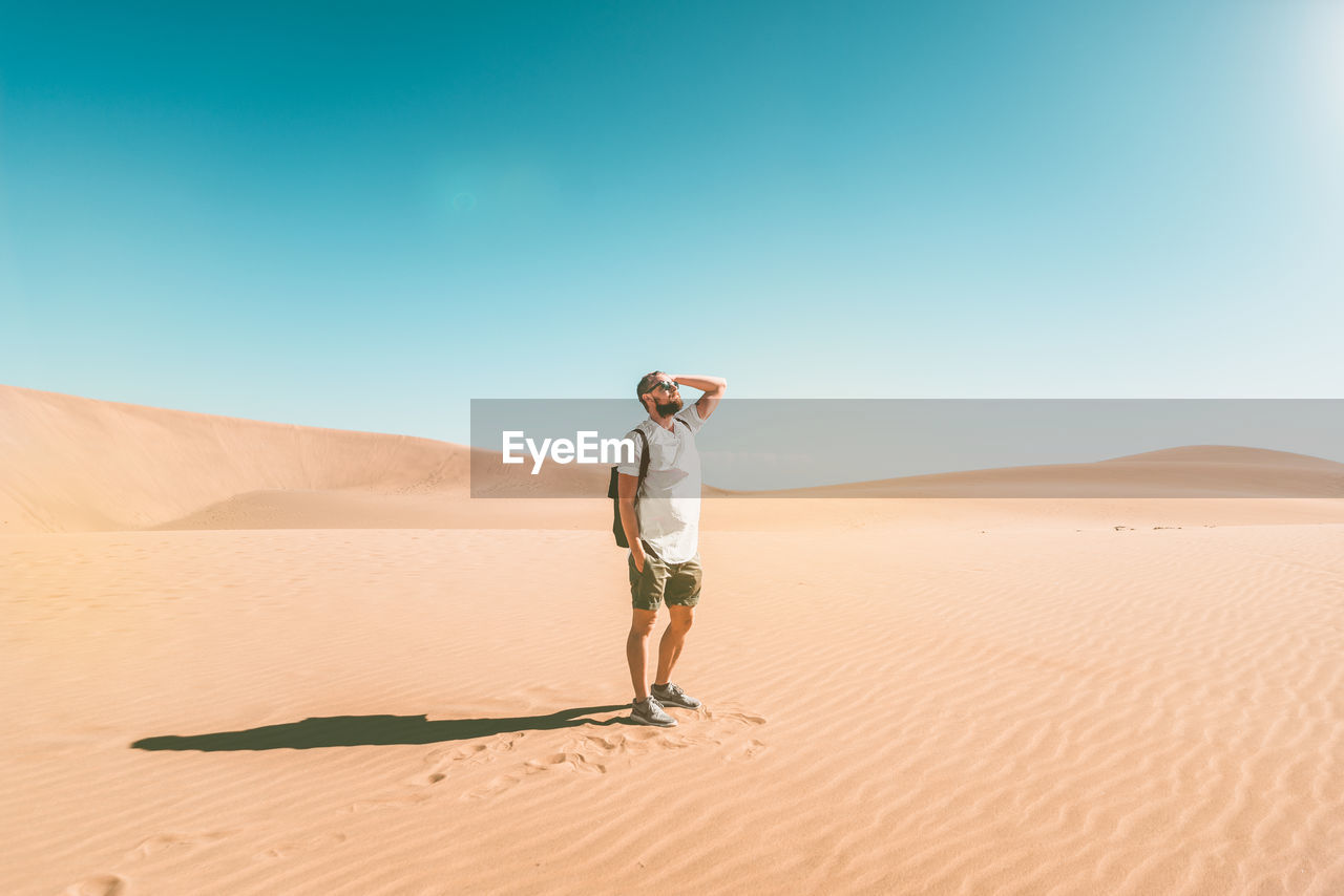 Full length of young man standing in desert against clear sky