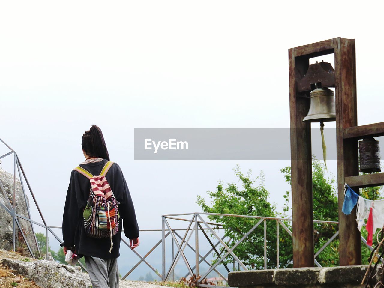 Rear view of woman with backpack walking by bell against clear sky