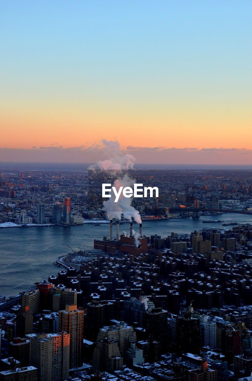 Aerial view of city by sea against clear sky during sunset