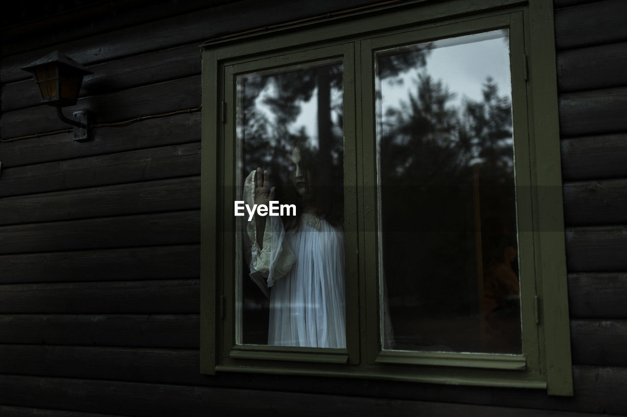 Female ghost looking through glass window of haunted cabin