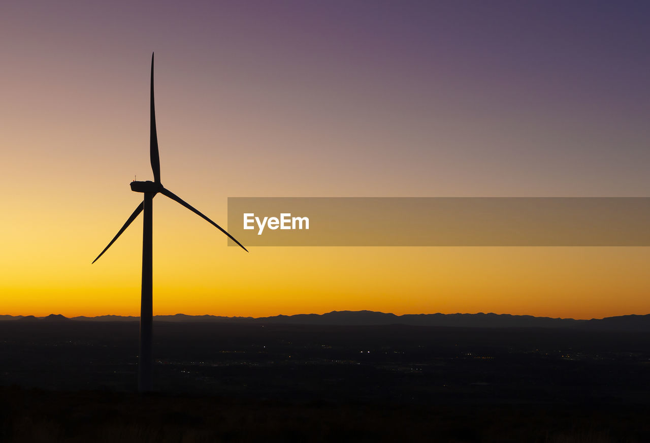 Wind turbines in field against sunset sky