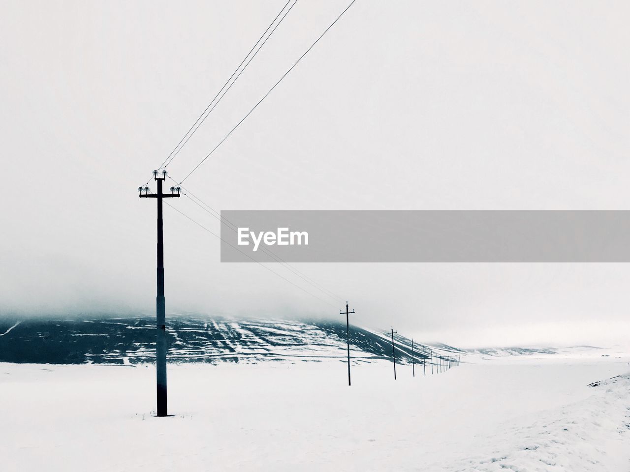 ELECTRICITY PYLON ON SNOW COVERED LAND AGAINST SKY