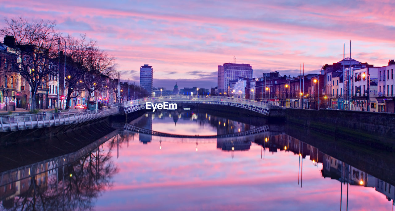 Bridge over river in city against sky at sunset